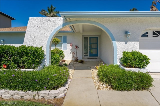 view of exterior entry featuring an attached garage and stucco siding