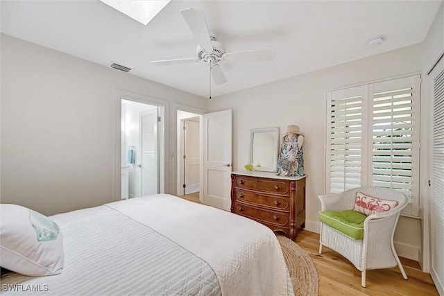 bedroom featuring a skylight, baseboards, visible vents, a ceiling fan, and light wood-style floors