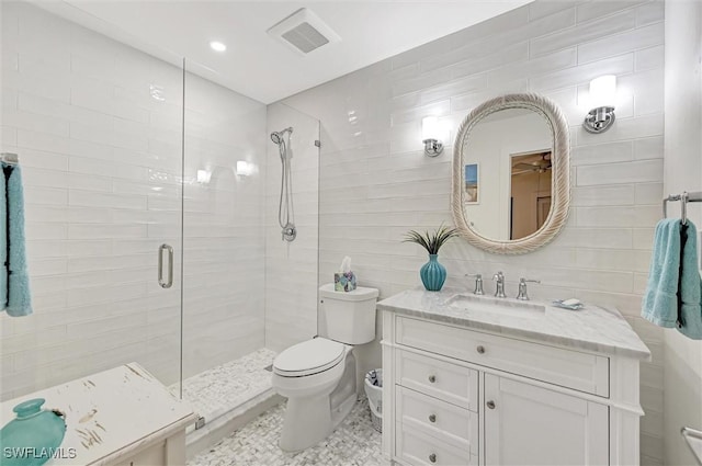 bathroom with toilet, visible vents, vanity, tile walls, and a shower stall