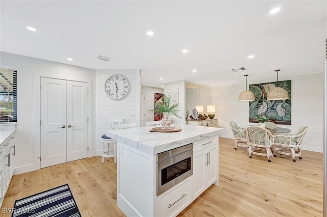 kitchen featuring a center island, pendant lighting, stainless steel microwave, light wood-style floors, and white cabinets