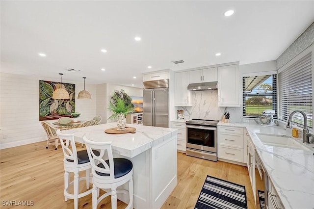 kitchen with white cabinets, decorative light fixtures, stainless steel appliances, under cabinet range hood, and a sink