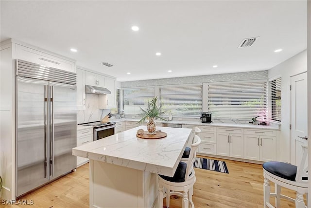 kitchen with visible vents, appliances with stainless steel finishes, white cabinetry, a kitchen island, and under cabinet range hood