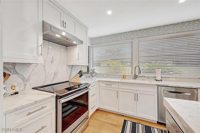 kitchen with under cabinet range hood, stainless steel appliances, a sink, white cabinetry, and light stone countertops