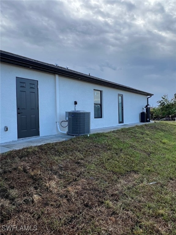 rear view of house with central AC, a lawn, and stucco siding