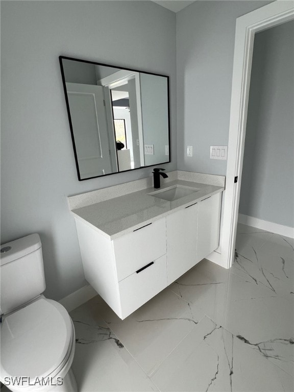 bathroom with toilet, marble finish floor, baseboards, and vanity