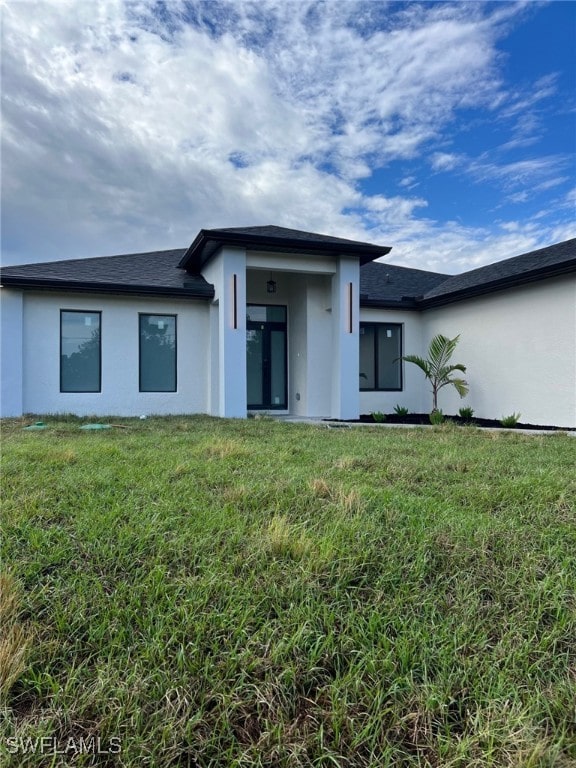 rear view of house with a lawn and stucco siding