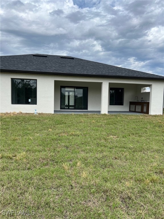 back of property with roof with shingles, a patio area, a lawn, and stucco siding