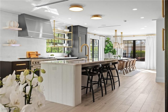 kitchen with a sink, light wood-type flooring, wall chimney range hood, open shelves, and backsplash