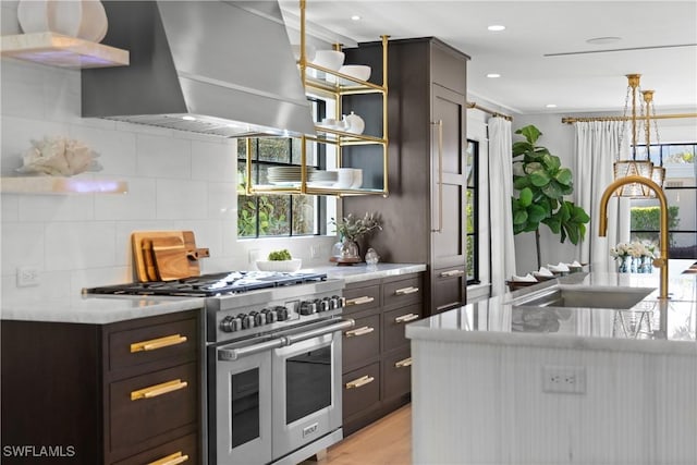 kitchen featuring open shelves, decorative backsplash, a sink, double oven range, and wall chimney exhaust hood