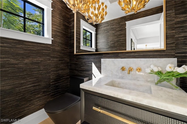 half bathroom with toilet, vanity, and a notable chandelier