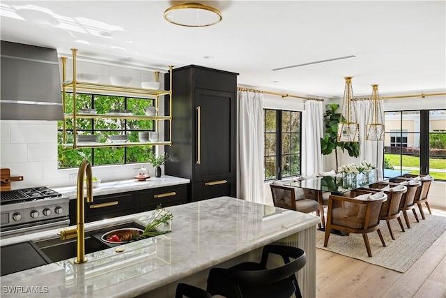 kitchen with dark cabinets, light wood-type flooring, paneled refrigerator, and light stone counters