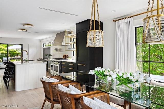 kitchen with decorative backsplash, range with two ovens, light wood-style flooring, wall chimney range hood, and a sink