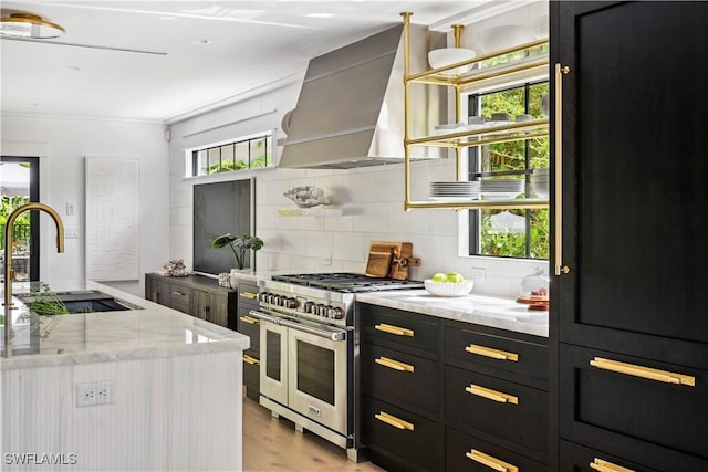 kitchen featuring a sink, dark cabinetry, wall chimney range hood, double oven range, and a wealth of natural light