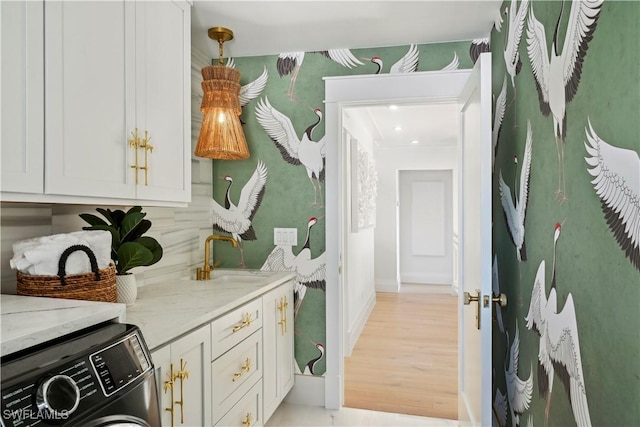 laundry room featuring light wood-type flooring, cabinet space, a sink, and baseboards