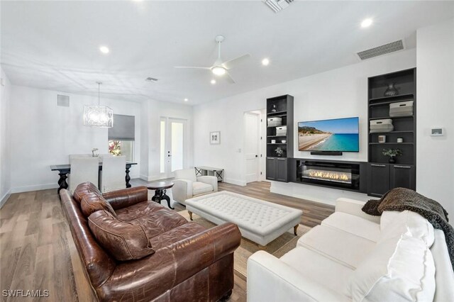 living area featuring light wood finished floors, a chandelier, recessed lighting, baseboards, and a ceiling fan