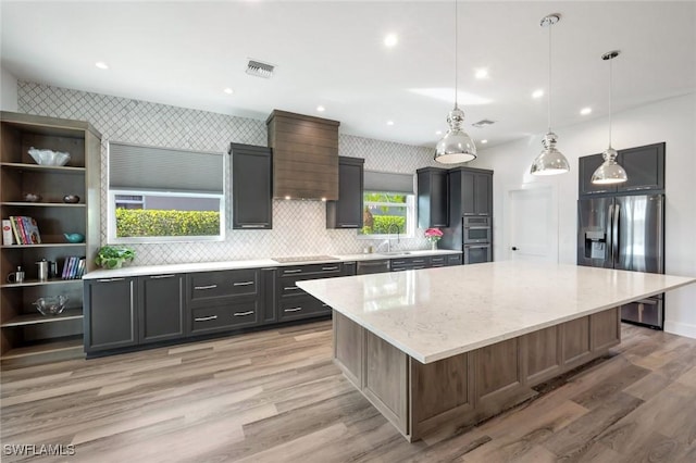 kitchen featuring stainless steel appliances, a large island, light wood-type flooring, a sink, and light stone countertops
