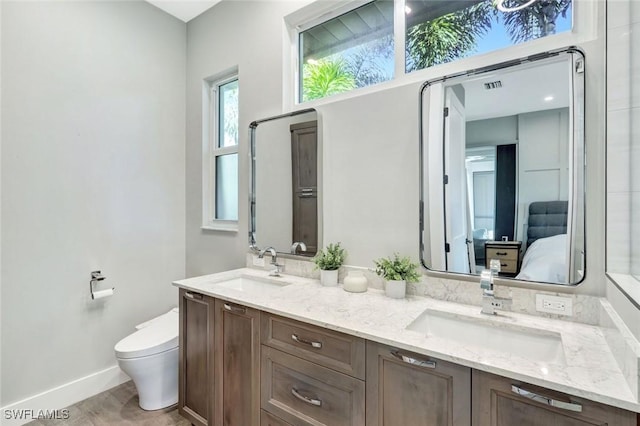 ensuite bathroom featuring toilet, baseboards, double vanity, and wood finished floors