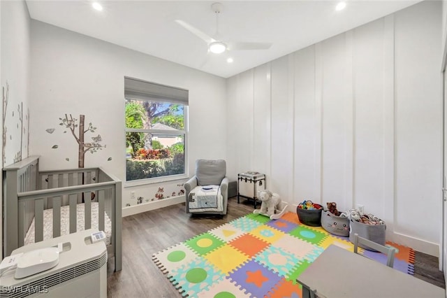 bedroom featuring a nursery area, wood finished floors, baseboards, ceiling fan, and recessed lighting