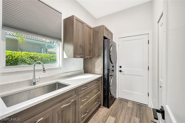 kitchen featuring stacked washing machine and dryer, a sink, light wood-style flooring, and light countertops