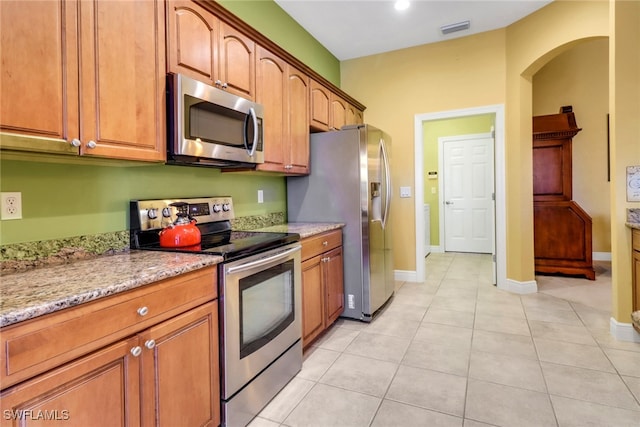 kitchen with arched walkways, light tile patterned floors, visible vents, appliances with stainless steel finishes, and light stone countertops