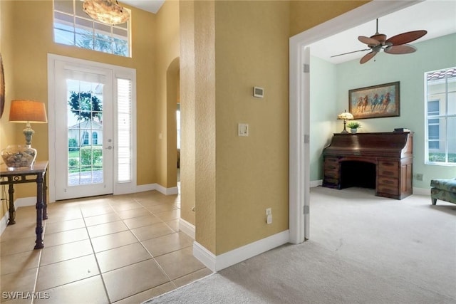 carpeted foyer entrance with baseboards, arched walkways, ceiling fan, and tile patterned flooring