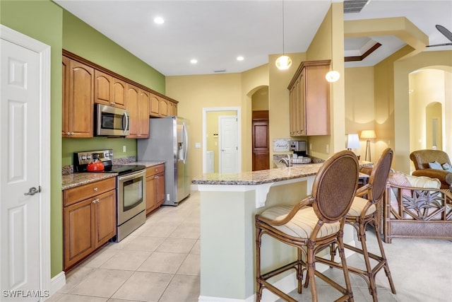 kitchen featuring arched walkways, stainless steel appliances, light stone counters, and a kitchen breakfast bar