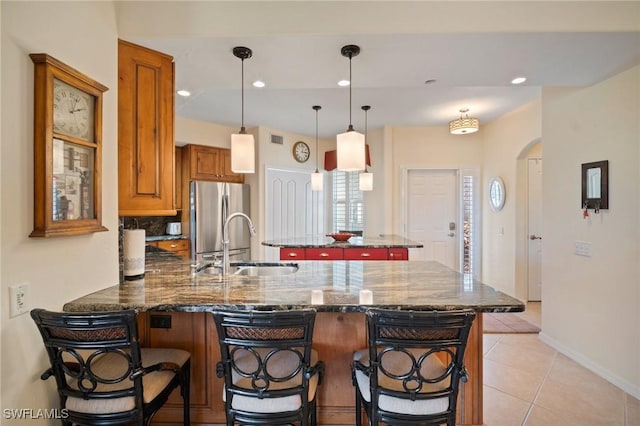 kitchen with arched walkways, brown cabinetry, freestanding refrigerator, a sink, and a peninsula