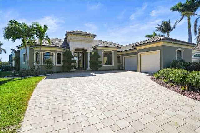 mediterranean / spanish-style home featuring stucco siding, decorative driveway, a front lawn, and an attached garage