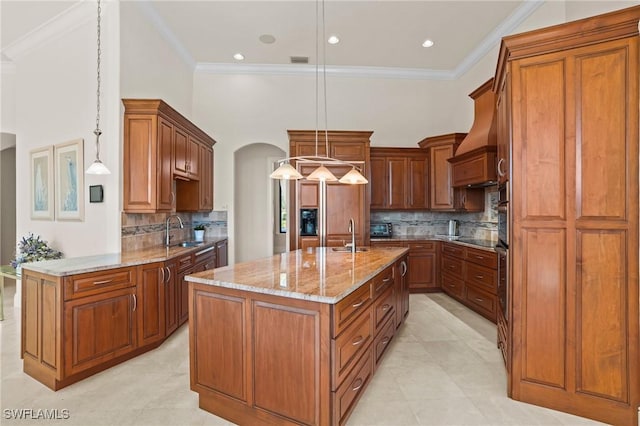 kitchen with an island with sink, ornamental molding, a sink, light stone counters, and arched walkways