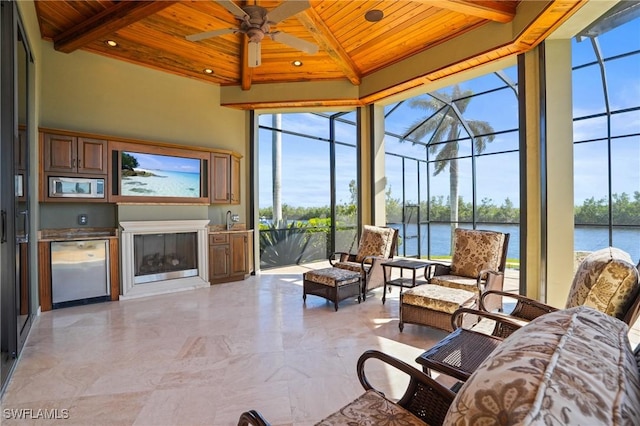 sunroom / solarium with ceiling fan, a water view, beamed ceiling, wood ceiling, and a glass covered fireplace