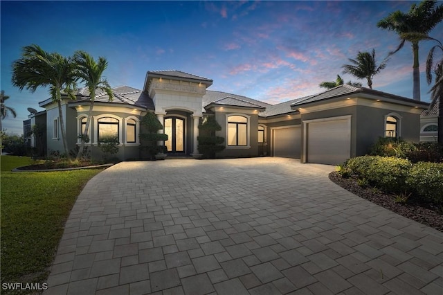 mediterranean / spanish-style home featuring a front lawn, a tiled roof, stucco siding, decorative driveway, and a garage