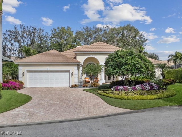 mediterranean / spanish house featuring a garage, decorative driveway, a tiled roof, and stucco siding