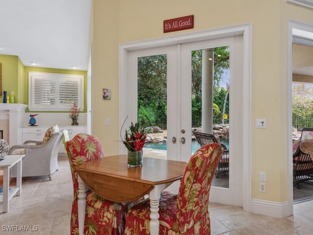 dining room featuring baseboards, french doors, a fireplace, and stone tile floors