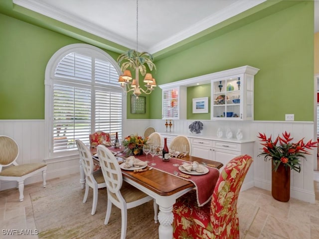 dining area with a chandelier, a wainscoted wall, and crown molding