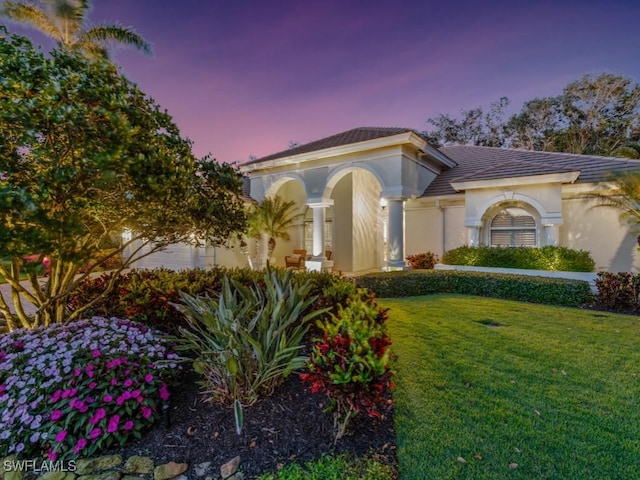 mediterranean / spanish house with an attached garage, a tile roof, a lawn, and stucco siding