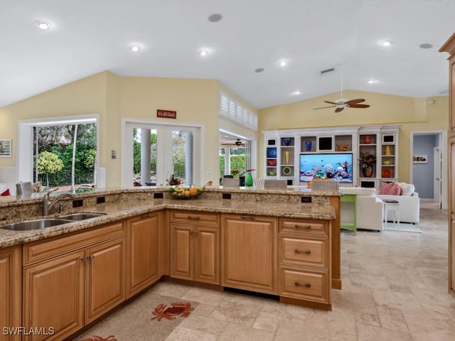 kitchen with lofted ceiling, recessed lighting, a ceiling fan, a sink, and light stone countertops