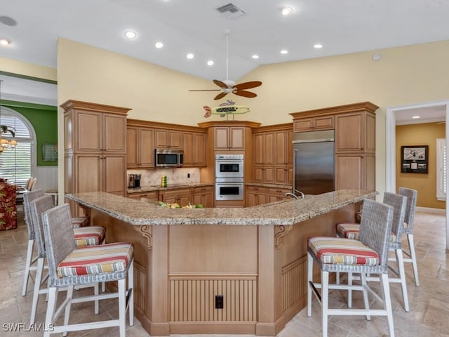 kitchen with visible vents, a spacious island, a breakfast bar area, stainless steel appliances, and stone tile flooring