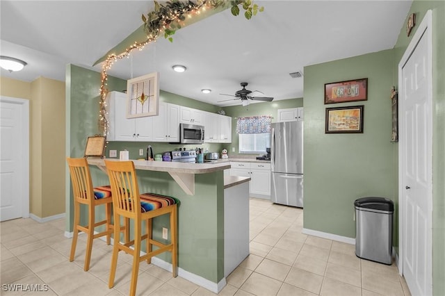 kitchen featuring a kitchen breakfast bar, a peninsula, stainless steel appliances, light countertops, and white cabinetry