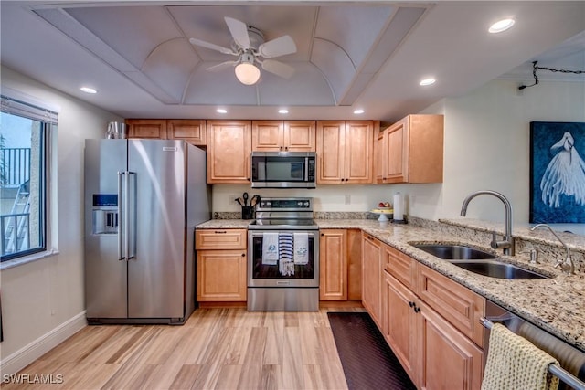 kitchen featuring light stone counters, a tray ceiling, appliances with stainless steel finishes, light wood-style floors, and a sink