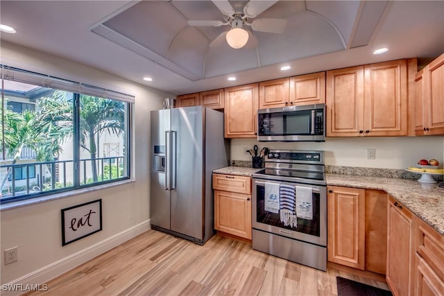 kitchen with a tray ceiling, appliances with stainless steel finishes, light wood-style floors, light stone countertops, and baseboards