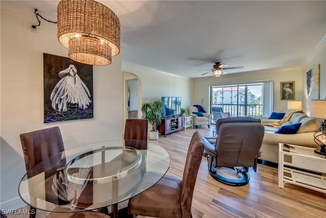 dining area featuring arched walkways, light wood-style flooring, ceiling fan with notable chandelier, baseboards, and ornamental molding