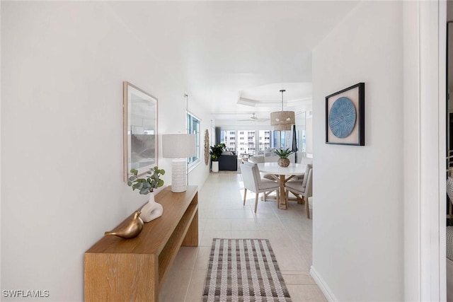 corridor with a tray ceiling, baseboards, and light tile patterned floors