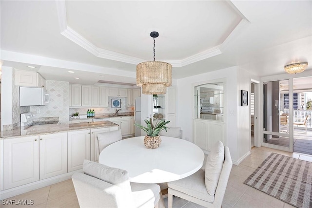 dining room with a tray ceiling, light tile patterned floors, ornamental molding, a chandelier, and baseboards