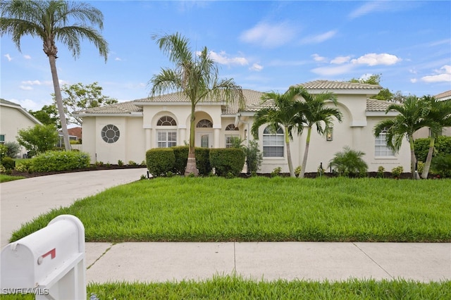 mediterranean / spanish house with a tiled roof, a front lawn, concrete driveway, and stucco siding