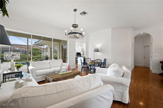 living area with arched walkways, visible vents, an inviting chandelier, ornamental molding, and wood finished floors