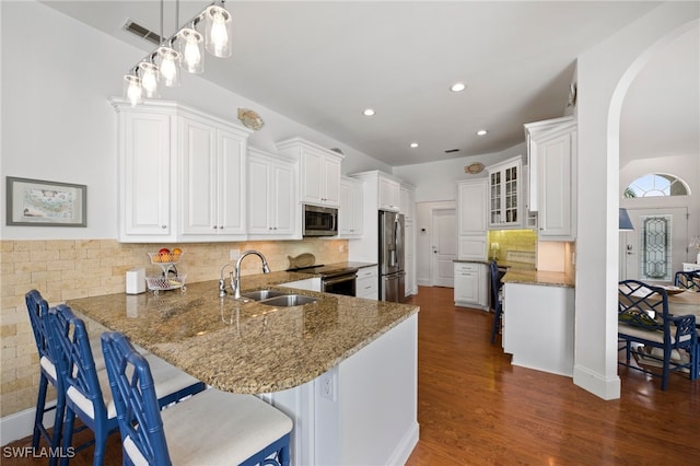 kitchen featuring stone counters, stainless steel appliances, a breakfast bar, a peninsula, and a sink