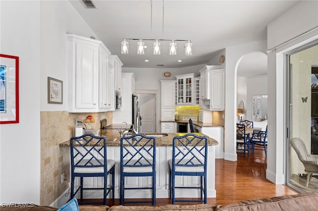 kitchen featuring visible vents, arched walkways, wood finished floors, a peninsula, and white cabinetry
