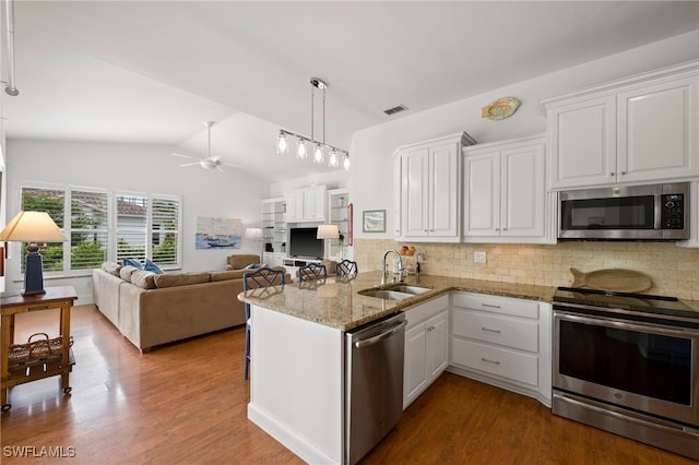 kitchen featuring a peninsula, wood finished floors, a sink, white cabinetry, and appliances with stainless steel finishes