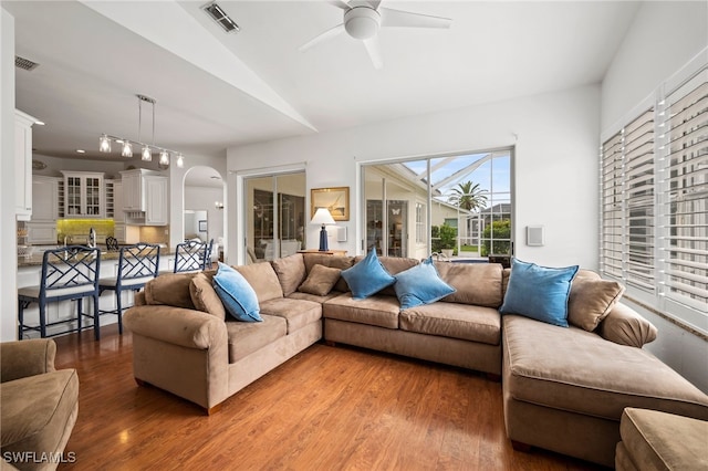 living area featuring ceiling fan, light wood finished floors, arched walkways, and visible vents