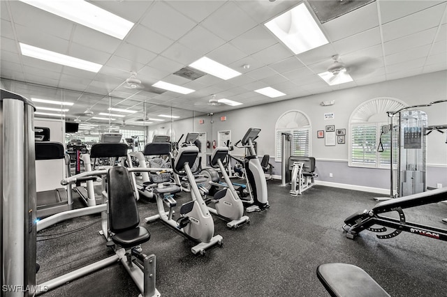 workout area with a paneled ceiling, baseboards, and a ceiling fan